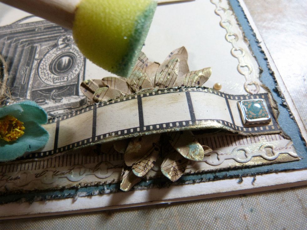 Finish of by gently dabbing some of the blue gold paint with a sponge applicator to the tips of the brown and grey flowers and the edges of the filmstrip and chains.