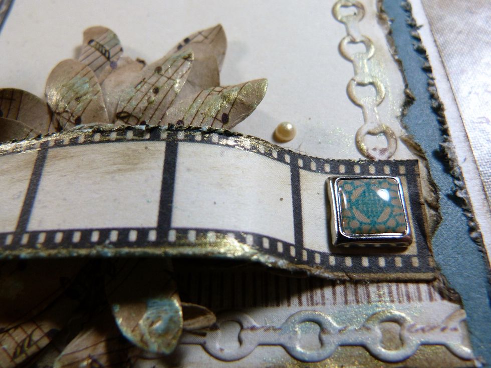 Finish off by gently dabbing some of the Blue Gold Art Alchemy paint with a sponge applicator to the tips of the brown & grey flowers & the edges of filmstrip & chains.