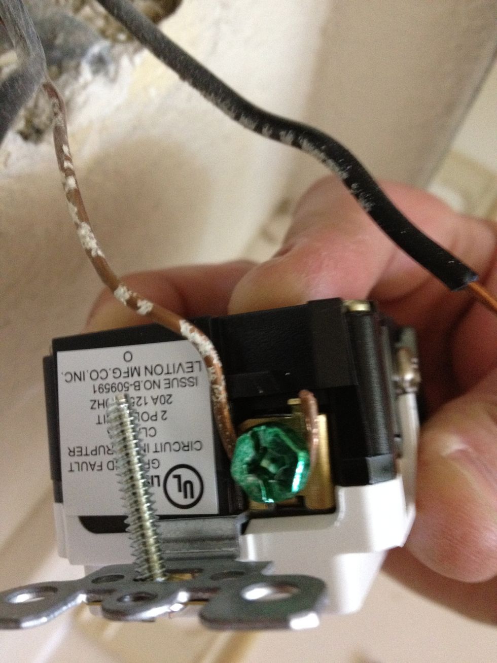 First connect the ground wire to the green screw at the bottom of the outlet. Wrap it around the screw and the tighten to lock the wire in place.