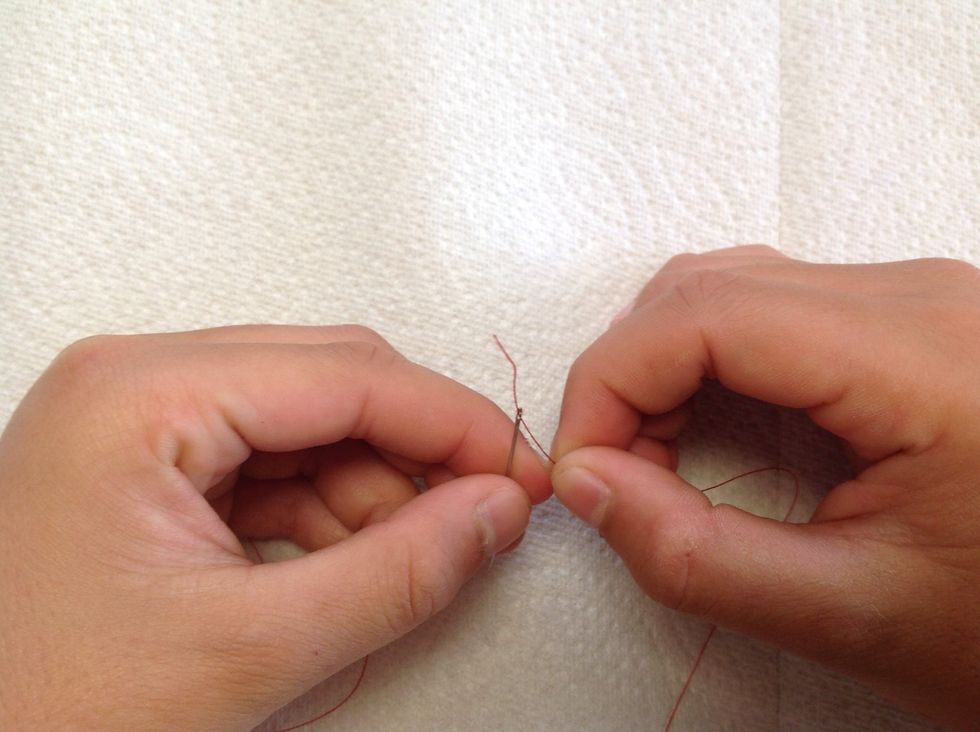First, hold the needle pointy side down, and poke the thread through the eye.