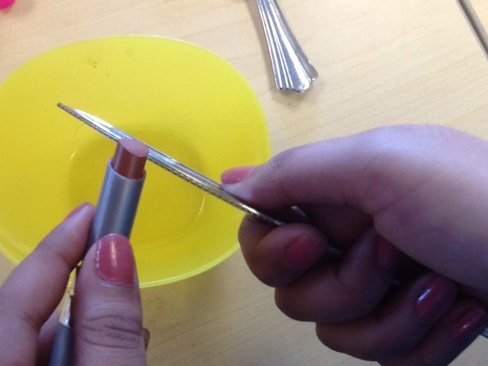 First, take the bowl and the butter knife and cut a little bit of the lipstick and put it into the bowl.
