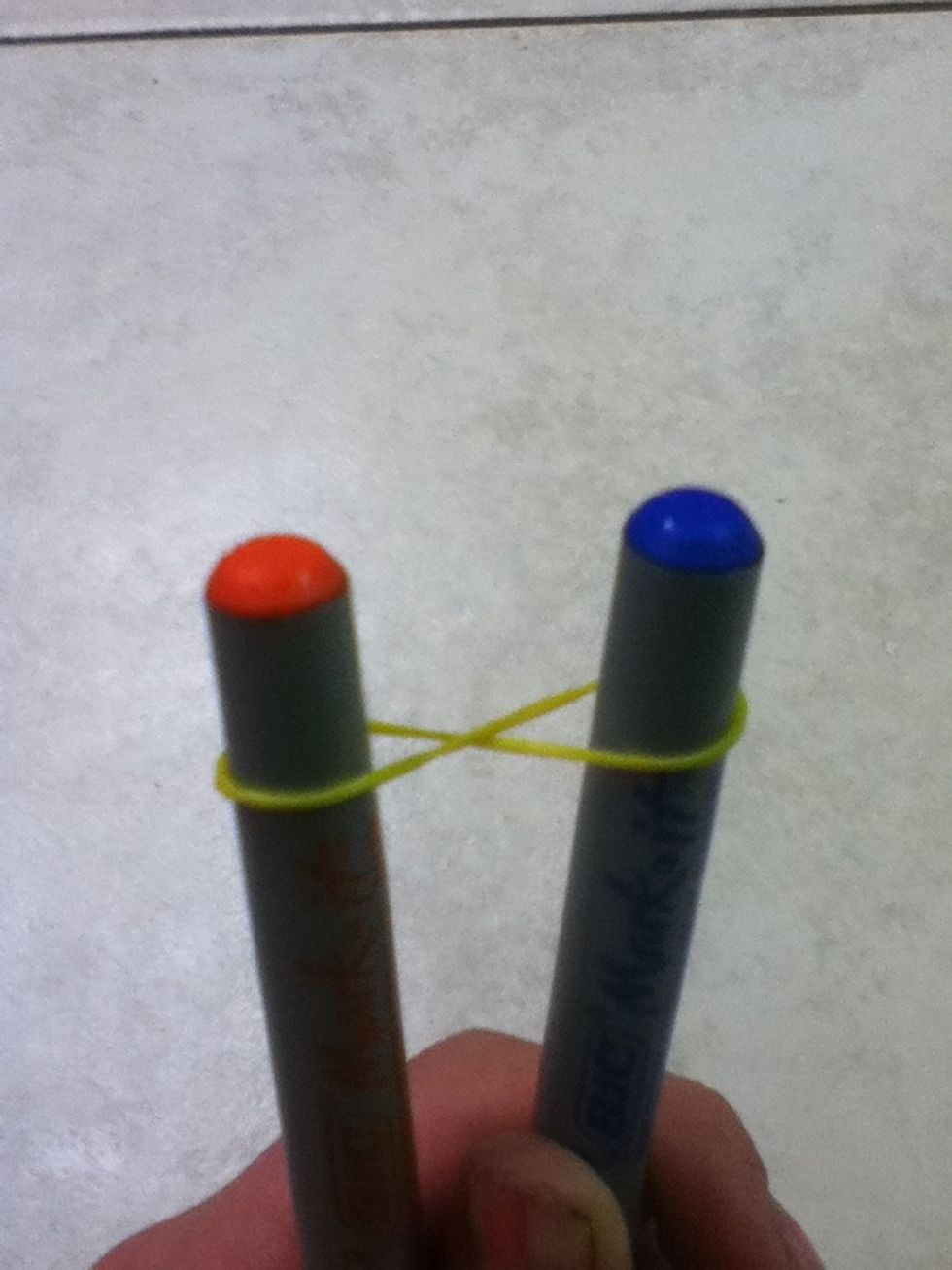 First, Twist the first rubberband on the sharpies