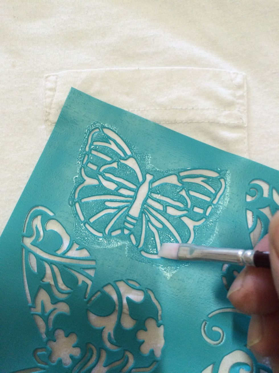 First using a small brush gently brush the glue on being carful to keep it from going under the stencil