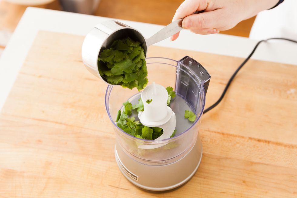 First, we'll make the cilantro dipping sauce. Add 3/4 cup of cilantro leaves to food processor.