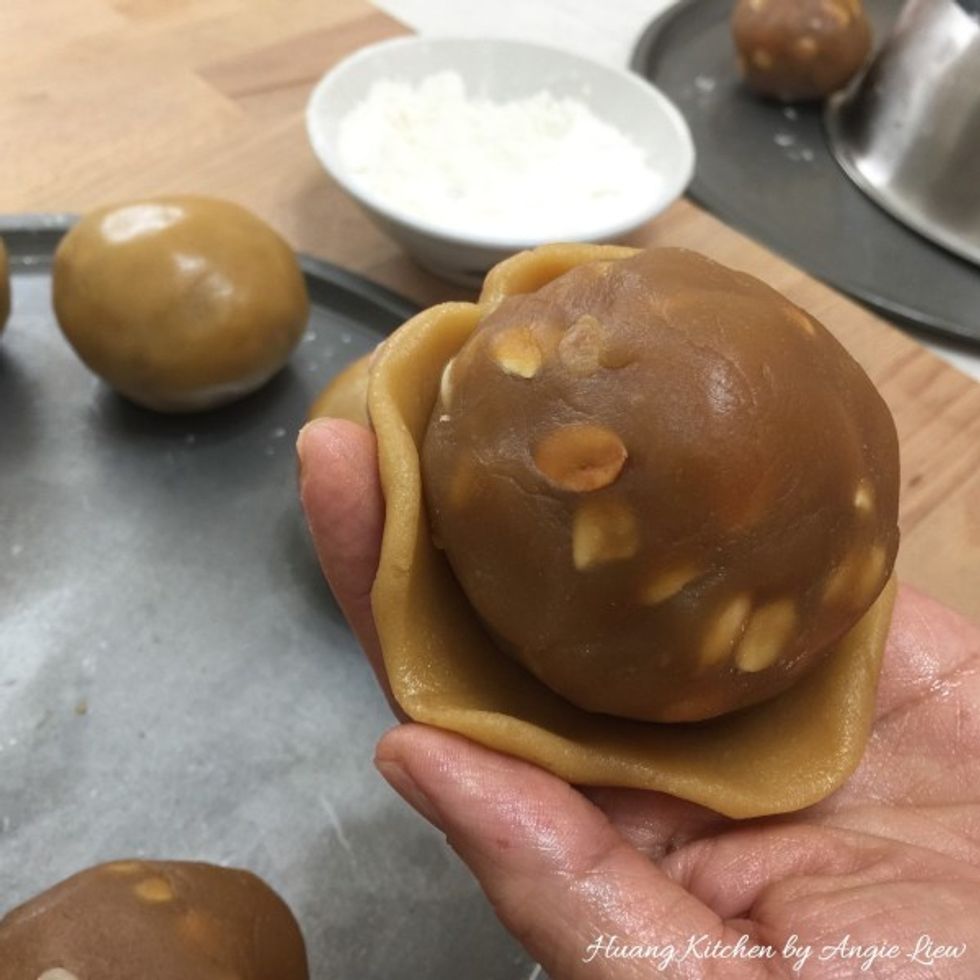 Flatten dough skin on palm of hand. Then flatten further using your fingertips. Put lotus paste ball onto the flattened dough and enclose filling by gently pressing edges until filling is sealed.