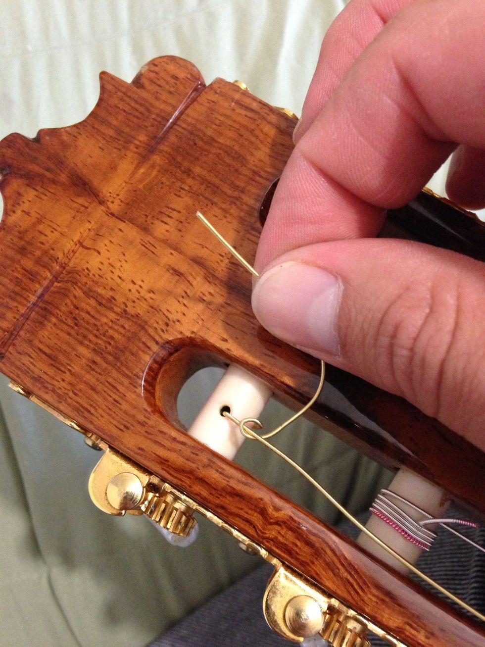 Flip the string under itself. Thus, it will remain tied while we turn the tuning peg.