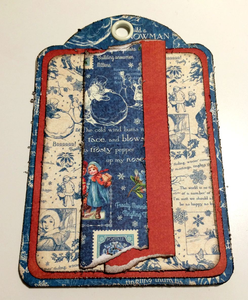 Foam square the red strip of paper 1" from the right and 1/2" from the bottom of the tag. Foam square the blue patterned paper 1" from the left and 1/2" from the bottom of the tag.