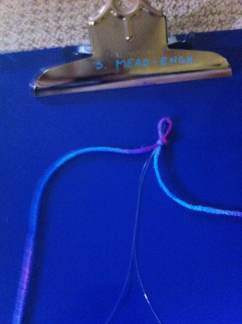 Fold both the clear string and yarn in half then tie a knot where the loops are.