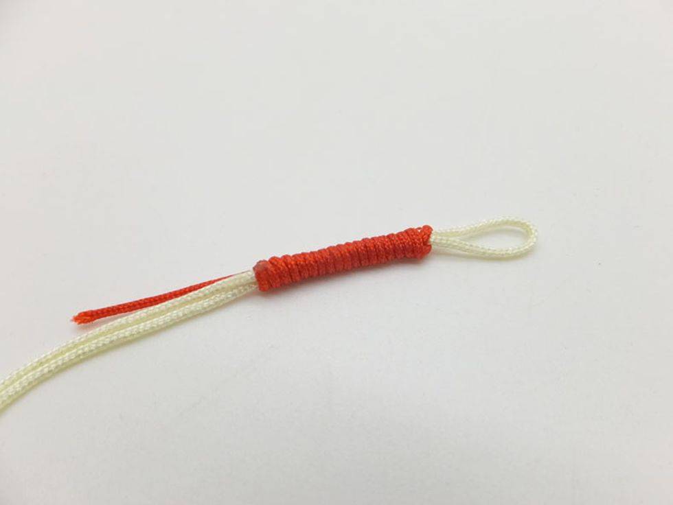 Fold the left cord and take hold of cord with your bracelet. Then take the right red working cord end and bring it up and over the holding yellowish cords again and again towards cord end position.