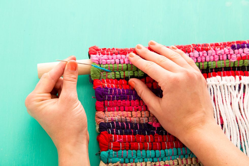 Fold the rug in half over the dowel, then use embroidery thread to stitch the rug in place.
