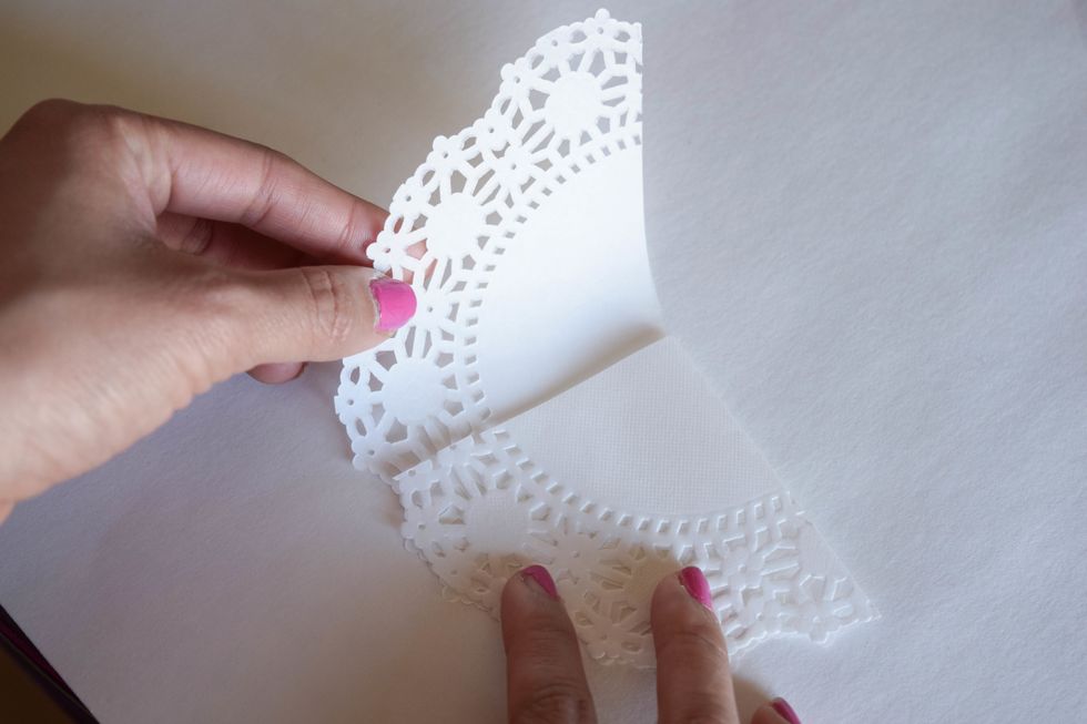 Fold the top left part of the doily down and over the part you just folded. You'll end up with a triangular shape with a rounded bottom.