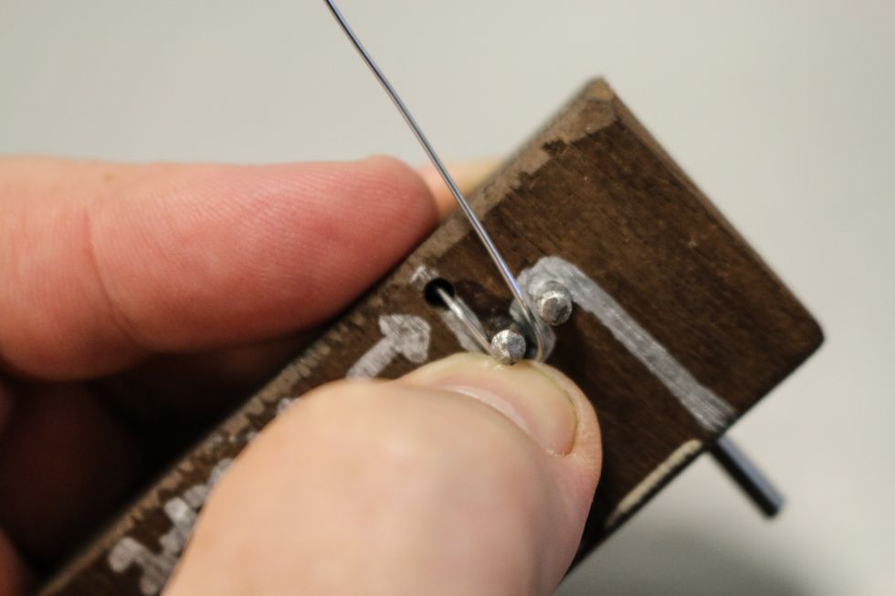 Following the direction line marked on the jig, hold down the starting end in the hole and start to bend the wire around the pins...