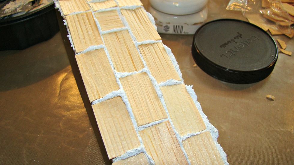 For dimension, using the texture paste mixture I pushed into place these wood pieces I got at the craft store. Let the paste ooze from the middle like grout. Set aside to dry.