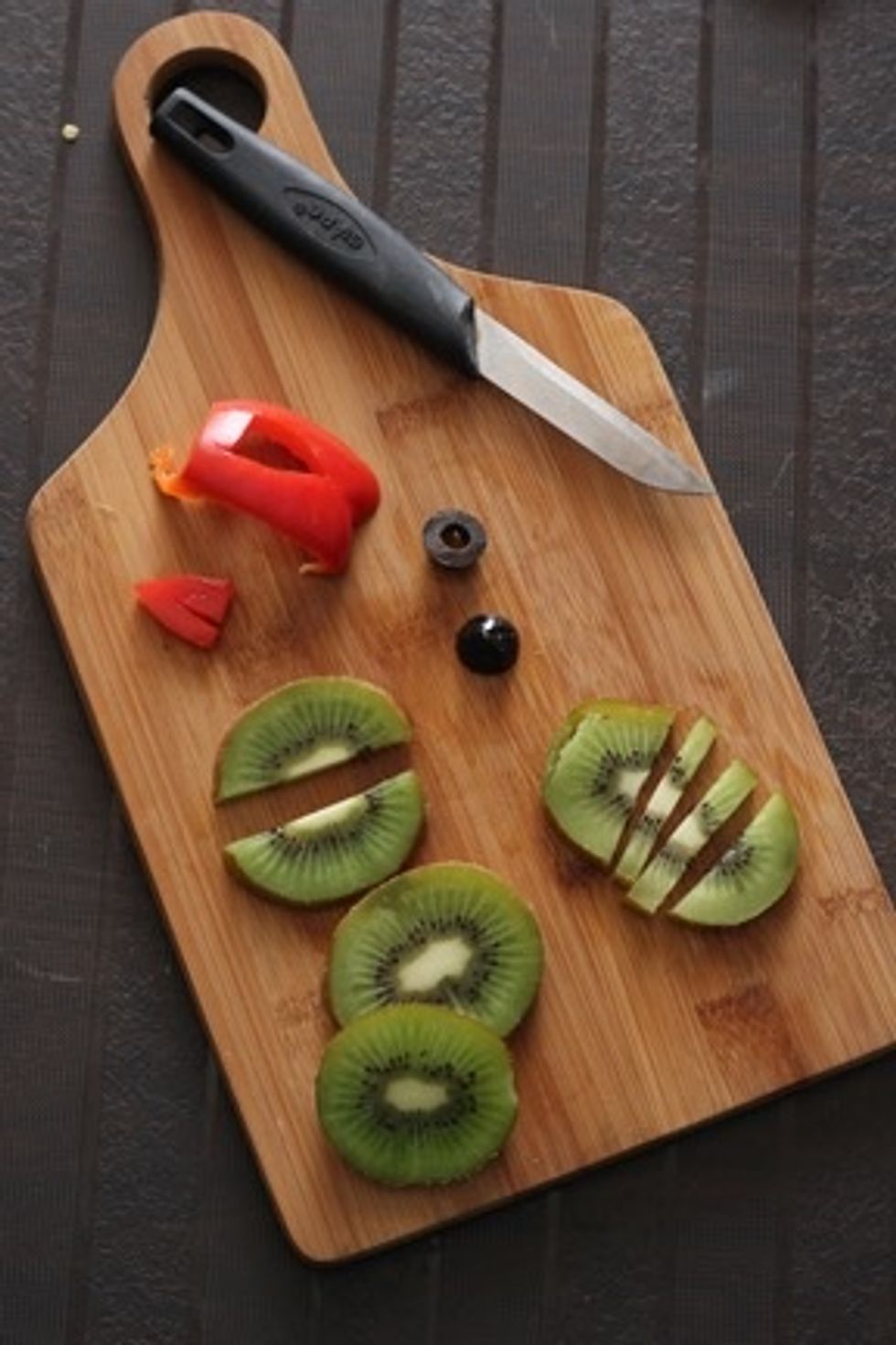 For the parrot -  Take  4 kiwi slices , divide the slices as shown in the pic. Cut out a small triangular piece for beak from red pepper . Divide olive into horizontal half.