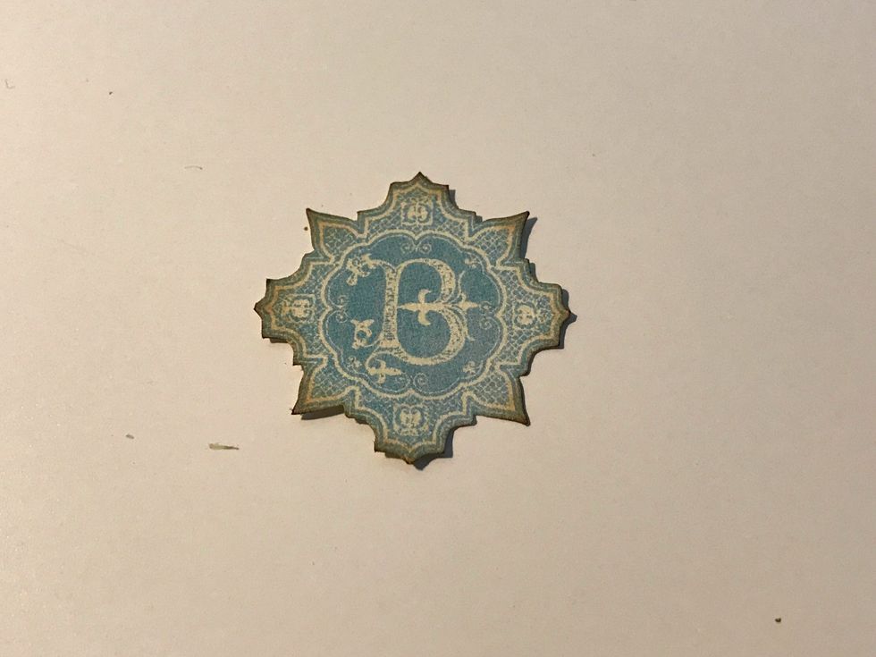 From the blue paper with B's on it, fussy cut one of the B's out. Ink the edges of the image using Vintage Photo Distress Ink and a blending tool with foam.