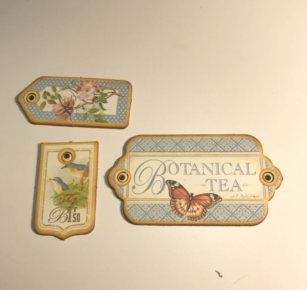 From the chipboard, punch out the Botanical Tea label, the bird banner and the rose tag. Ink the edges of the chipboard pieces using Vintage Photo Distress Ink.