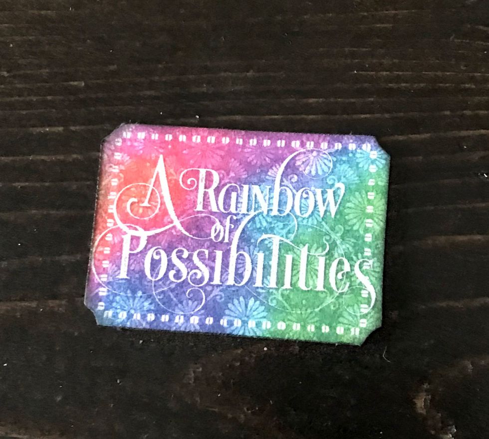 From the Tags and Pockets, punch out the "A Rainbow" piece. Distress the edges. Ink the edges with black ink.