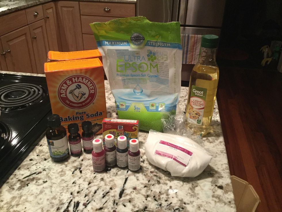 Gather all the supplies and ingredients, including 2 bowls, a whisk, measuring spoons, the bath bomb molds, baking soda, citric acid, Epsom salts, olive oil, water, essential oil, and food coloring.