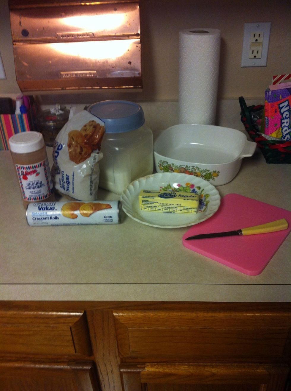 Gather together sugar, brown sugar, a roll of crescent rolls, ground cinnamon, butter/margarine, and the necessary tools to cut with and cook in.