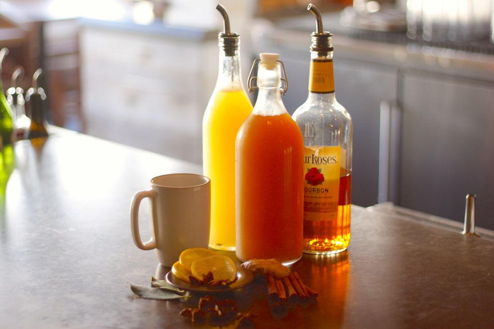 Gather your ingredients. Here we have lemon juice, Four Roses Bourbon, unfiltered apple cider, lemon wedges, ginger, cinnamon, anise, and bay leaves.