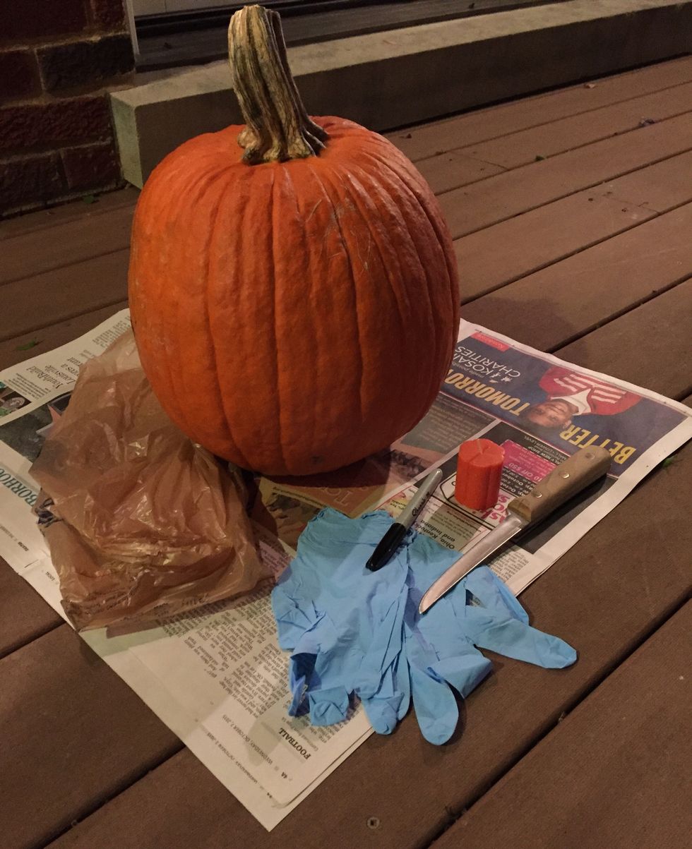 Gather your materials including a sharp knife, pumpkin, latex gloves, a Sharpie marker, plastic bag, small candle, a lighter, and newspaper.