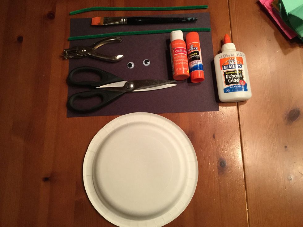 Gather your supplies, glue, paper plate, pipe cleaners (green), black paper, orange paint, paint brush, googly eyes, hole puncher and scissors.