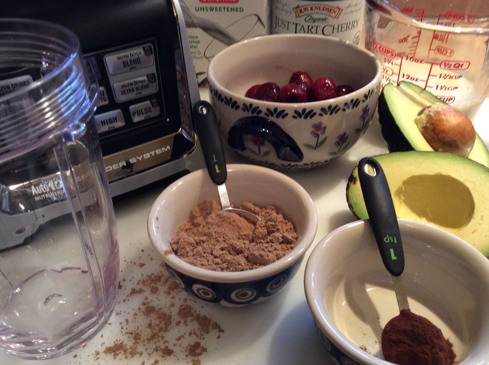 Gathered ingredients; 1 scoop chocolate protein powder, 1 tsp cocoa powder, 1/2 avocado, 3/4 c frozen cherries, 3/4 c almond milk and 1/4 c tart cherry juice.