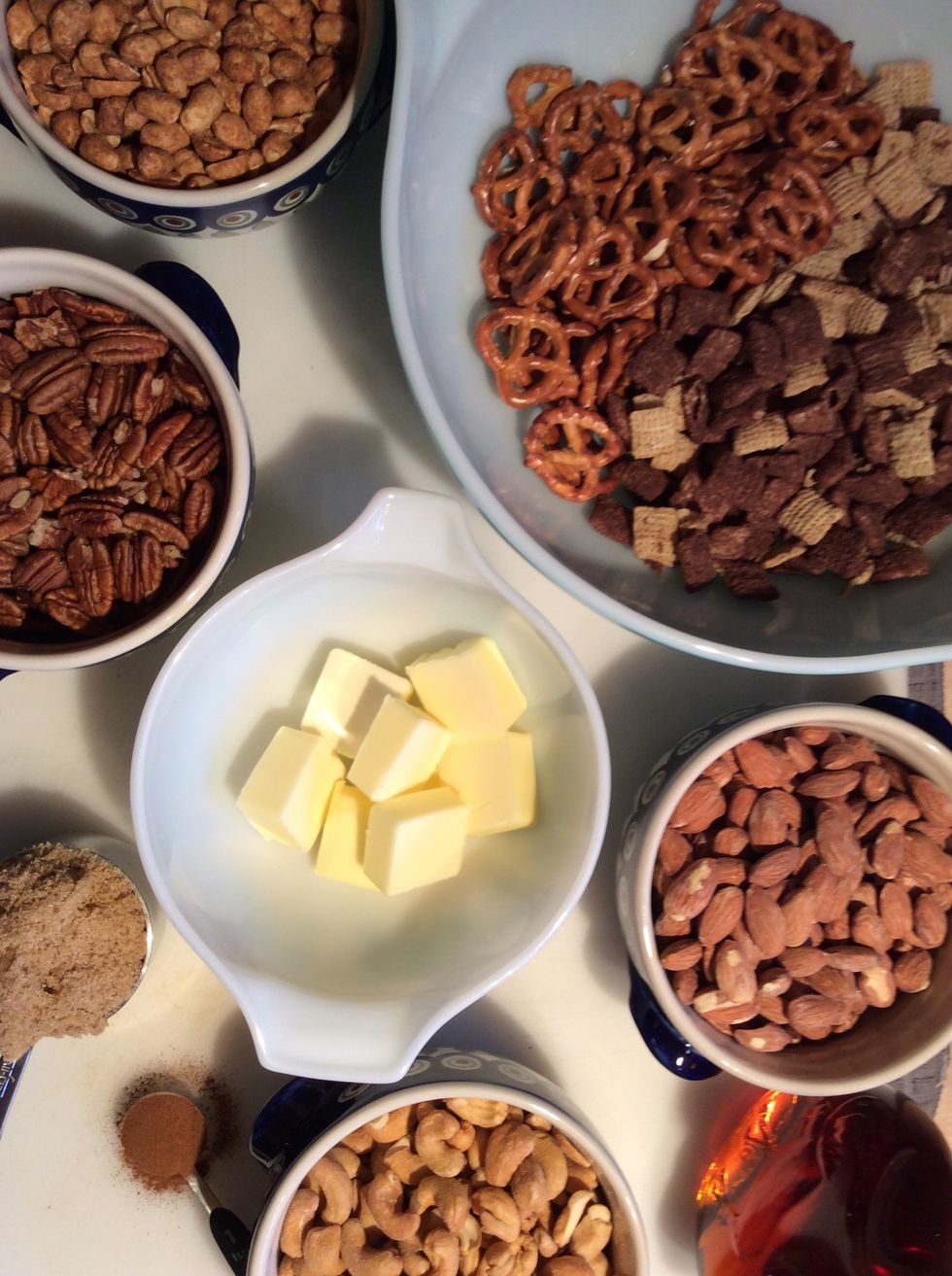 Gathered ingredients; butter, brown sugar, maple syrup, cinnamon, pecans, almonds, peanuts, cashews, pretzels and chocolate chex.