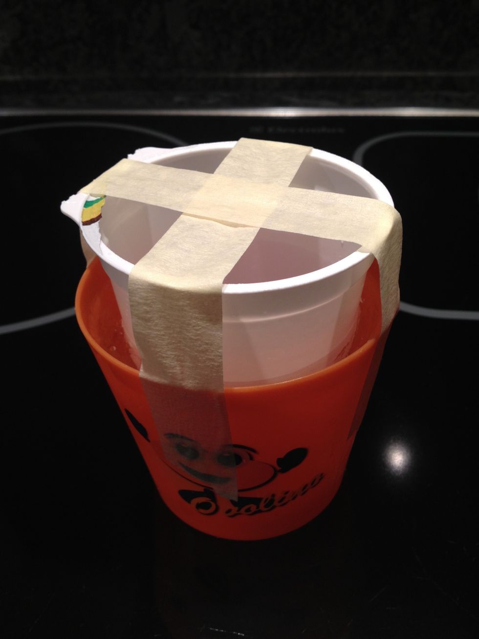 Gently put the smaller cup inside and press it down into the water. This creates a kind of cavity that's needed. Fix the cups with the tape so that the inner cup does not touch the outer one.