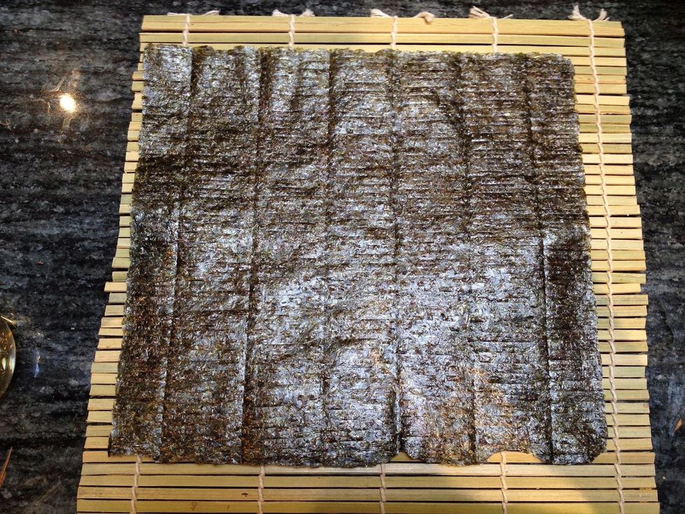 Get a sheet of nori (dried seaweed paper) and lay it with the shiny side facing down on the flat side of a sushi mat.