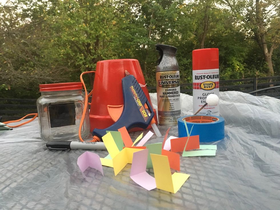 Get all your materials including a flower pot, red spray paint, black Sharpie, silver spray paint, a pencil, a foam ball, a big jar with a lid on it, and different color paper.
