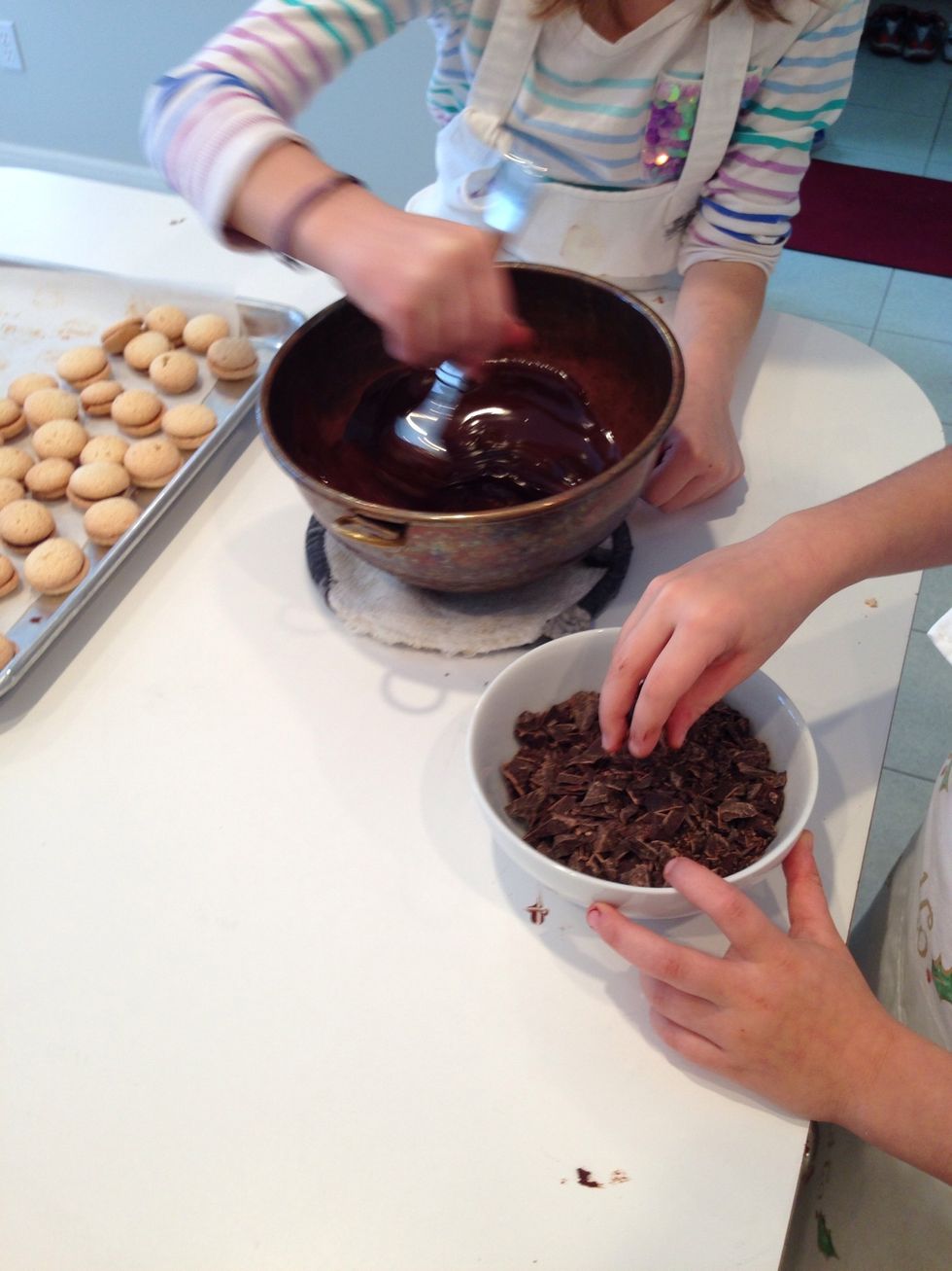 Get the chopped choc. and start adding. Hadley stirs constantly while Hildegard adds about 1/2 of that bowl. Take it's temp again. We want it to get down to low 90s. This is called tempering