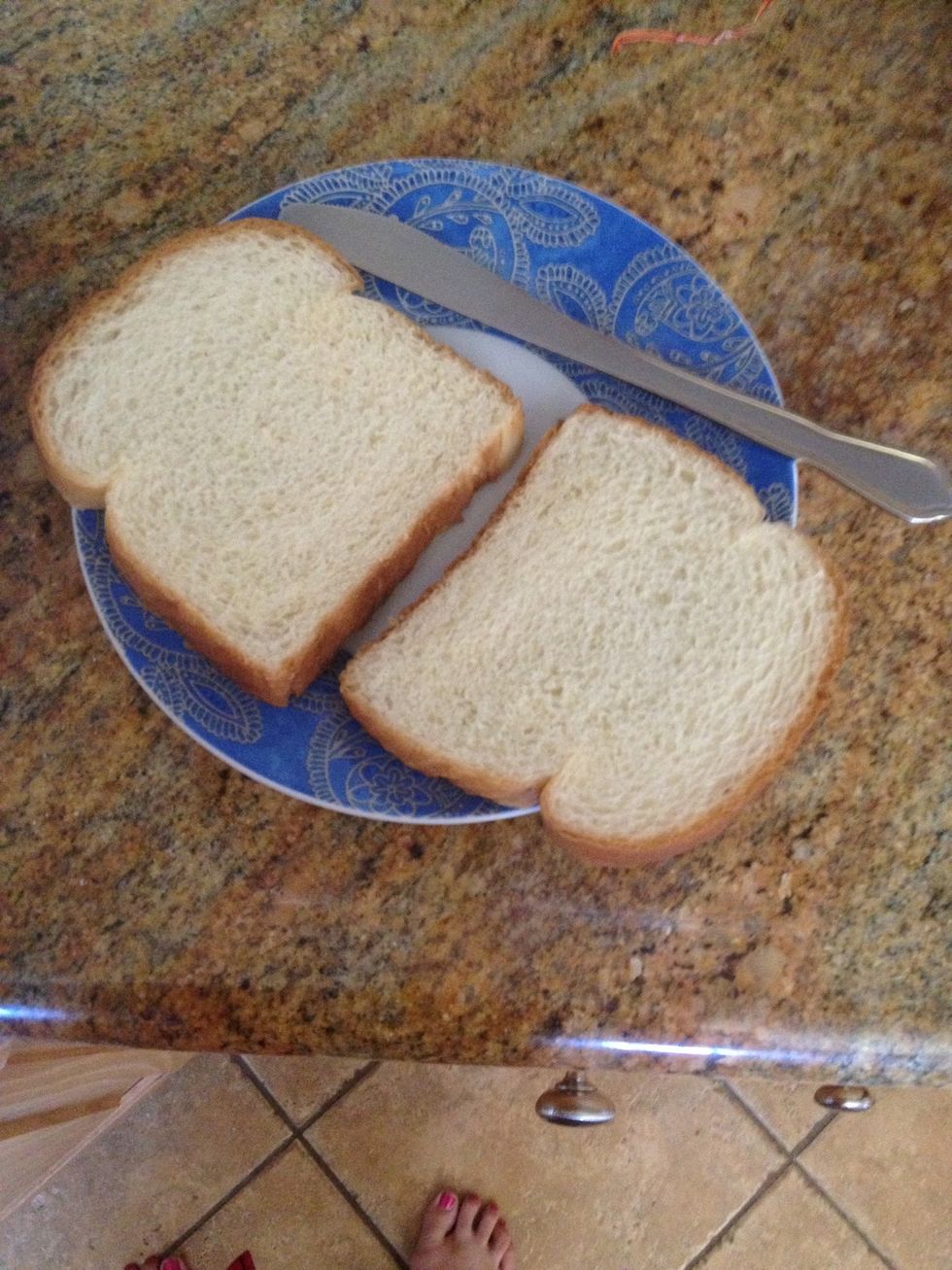 get two slices of bread ready on a plate with a butter knife