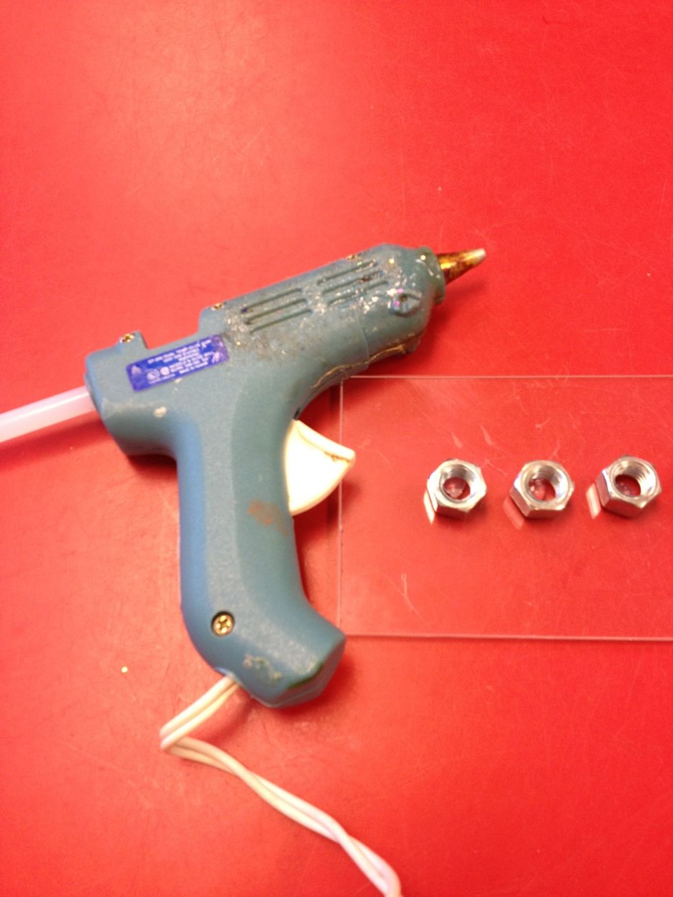 Glue 8 of the hex nuts onto the plexiglass in a straight line. Leave at least 11/2" space for the helper candle or Shamash. Only an adult should use the glue gun.