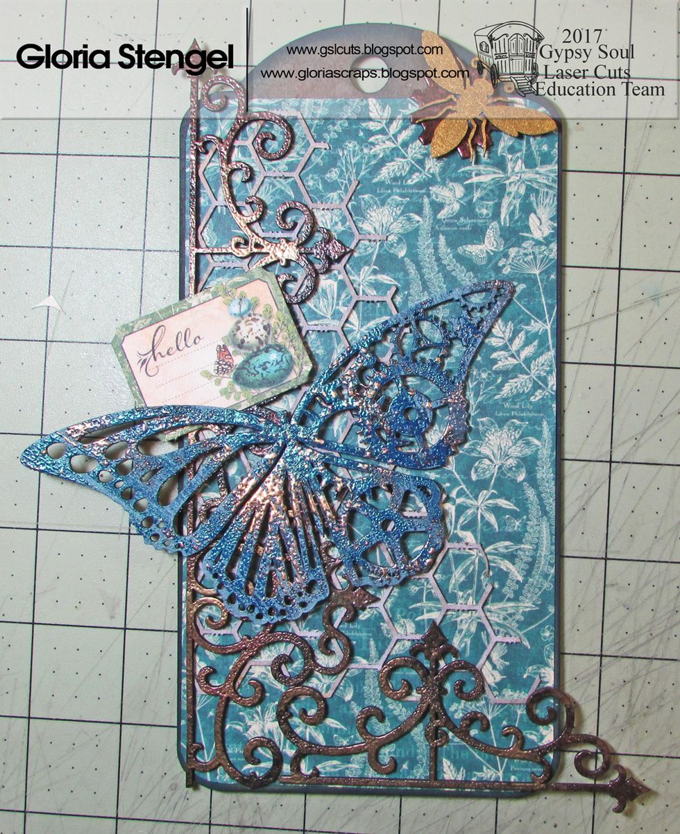 Glue a gear and the bee to the top of the tag. Add a decorative paper element to the left side of the tag, as shown.