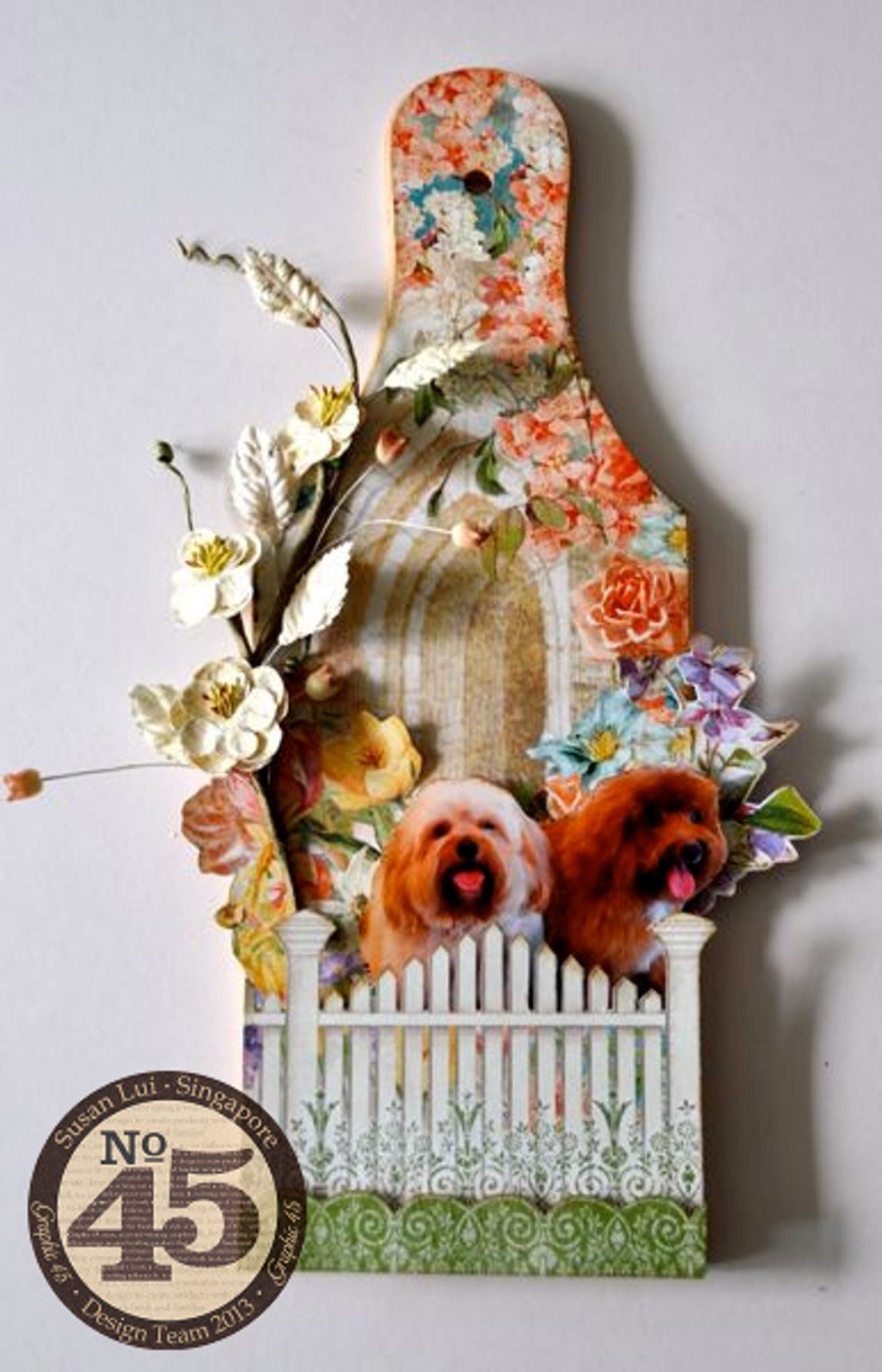 Glue a sprig of flowers to the left of the cheeseboard. Cut out the fence and attach it using 3D foam adhesive so that it looks like the subject is behind the fence.