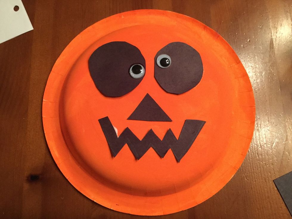 Glue the eyes, nose, and mouth onto the orange paper plate.
