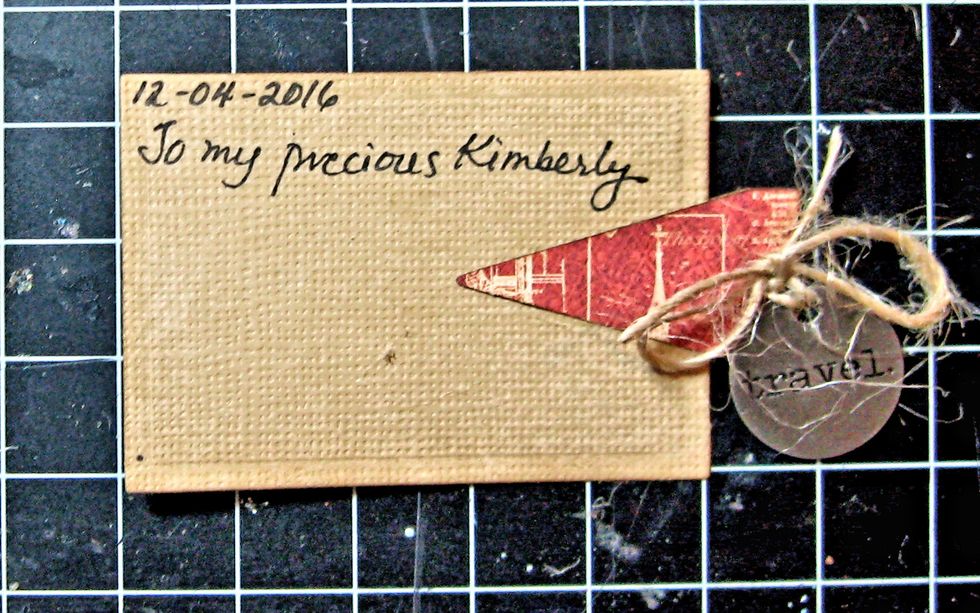 Glue the folded die cut over the right hand edge of mini postcard. Leave an edge so you can punch a hole and add a travel token, as seen here. Write your personal message here.