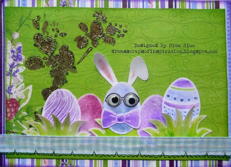 Glue the green paper onto the striped paper, attach a strip of blue ribbon from the Ephemera, on the bottom. Sew a zigzag along the ribbon. I used my sewing machine but you could also hand-stitch it.