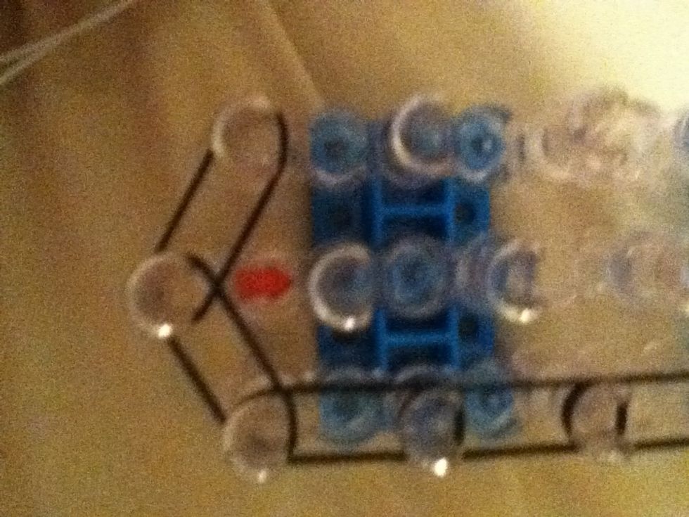 Go back to the red arrow and strech another rubber band from the first center peg to the first left peg.