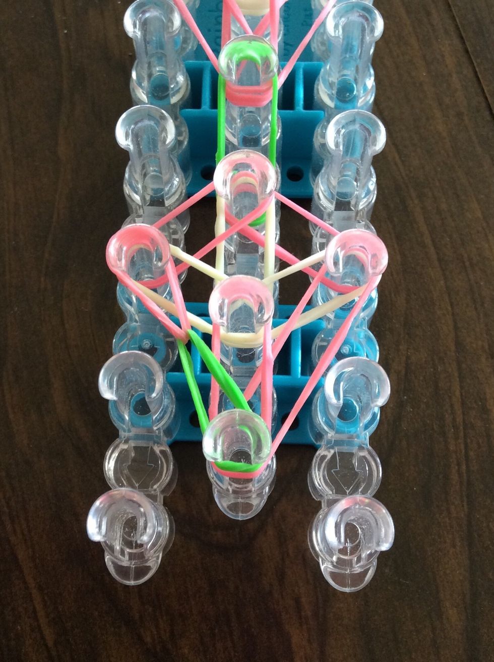 Go under the green band, take the top pink band, and bring to the third left peg.