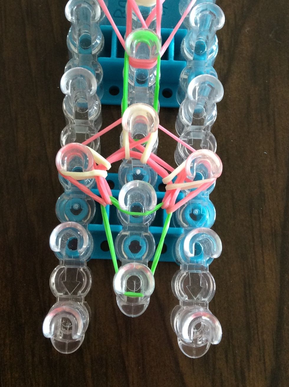 Go under the green band, take the white band, and bring it to the third middle peg.
