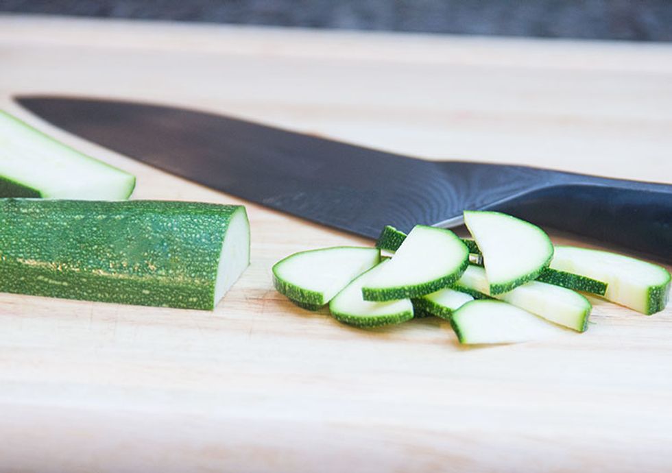 Grab a zucchini and chop off both ends. Cut the zucchini in half lengthwise and place each half flat-side-down on the cutting board for stability. And cut thin half-moon slices.