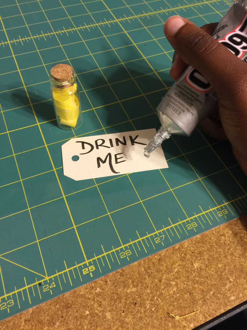 Grab your mini tag (feel free to write or print DRINK ME) and place a small line of E6000 adhesive on the corner.