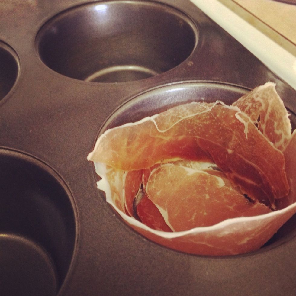 Grease the cupcake baking pan with butter. Create a bowl like shape in each section with strips of bacon or prosciutto.
