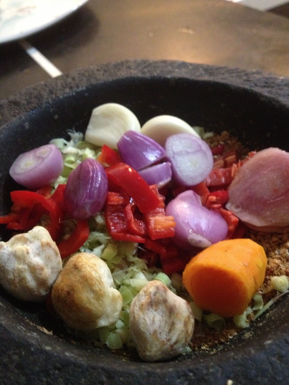Grind the coriander seeds first. Then, put all the spices into the mortar. Don't forget the prawn chili. Grind them. Alternatively, you can use a food processor to substitute the pestle and mortar.