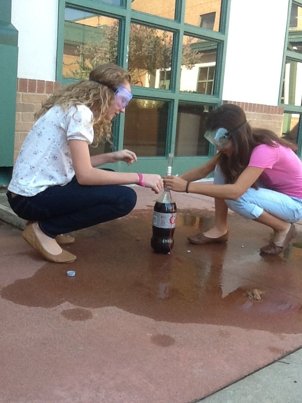Have the other person with safety goggles put the short end (part nearest to pin) into top of the open Diet Coke as quickly as possible