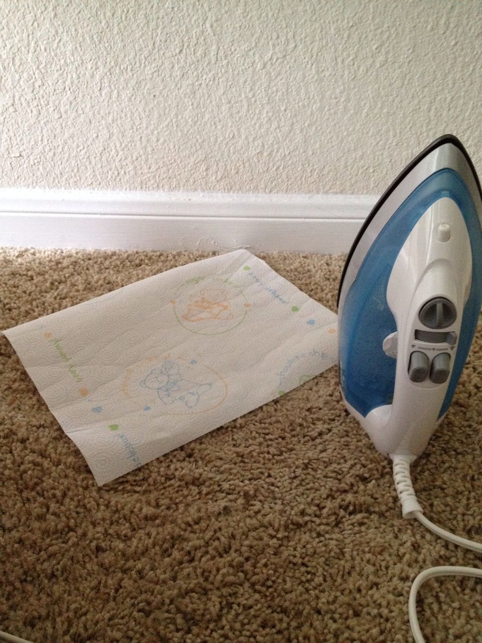 Heat your iron to a temp that won't burn the carpet. Then, place 1 piece of paper towel on top of the wax.
