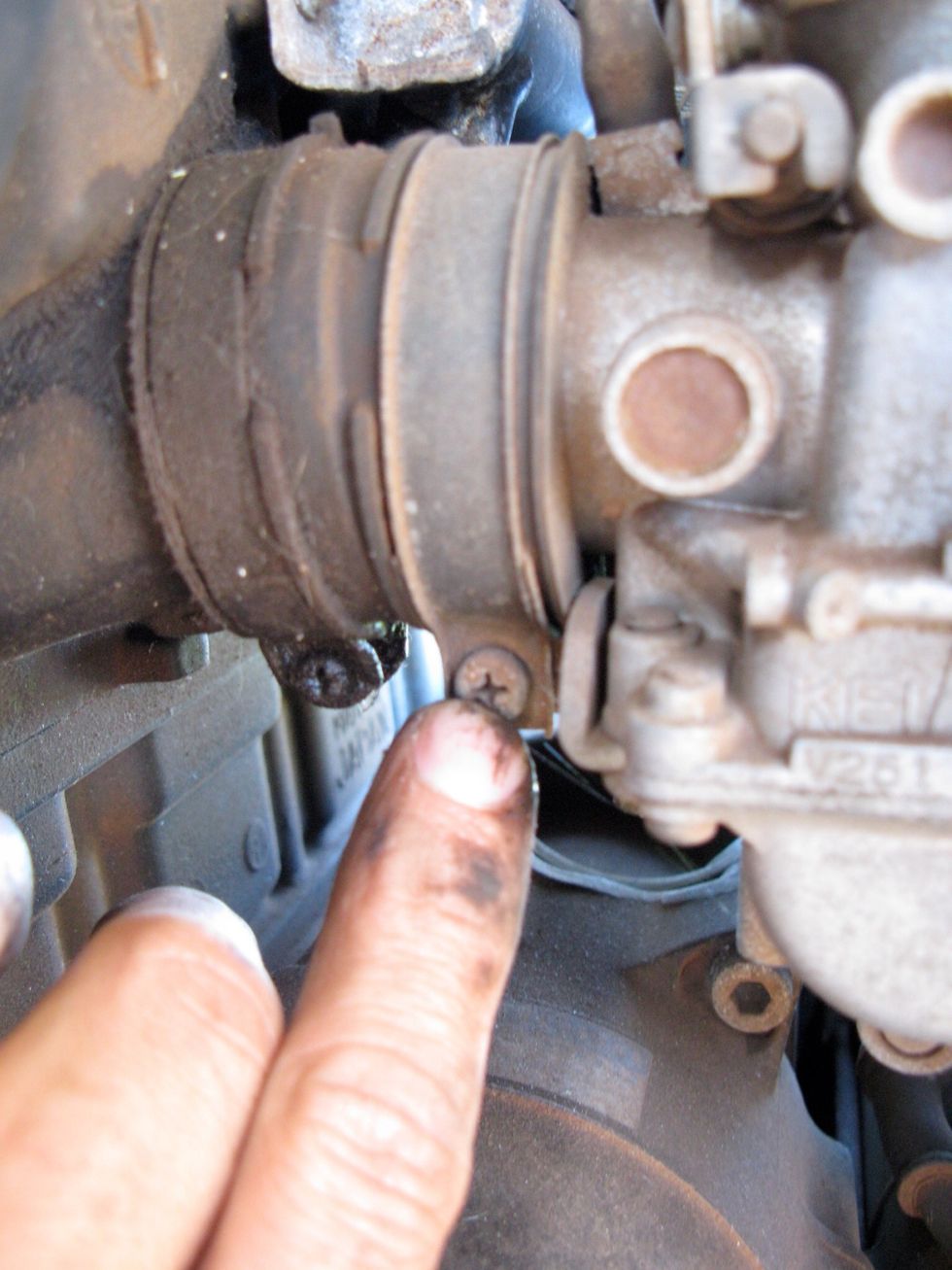 Here we go. The carbs are held in place by clamps on both sides. Use a Phillips on the engine side and loosen these up. You can reach two per side