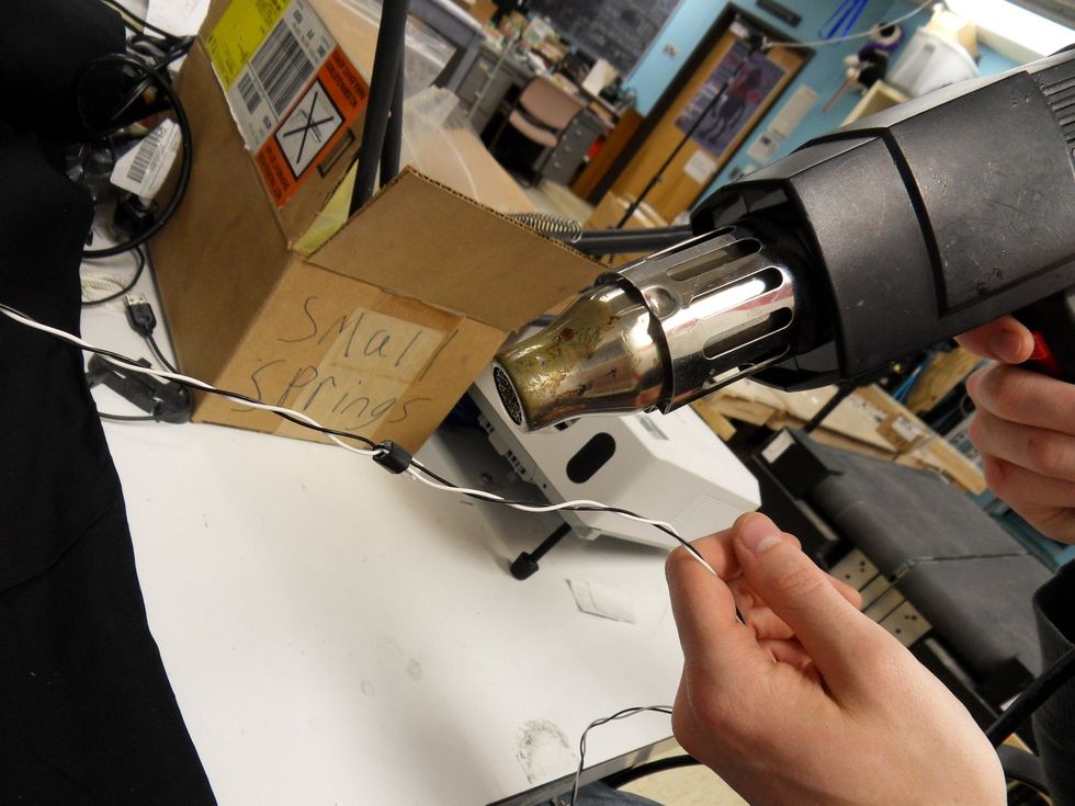 Hold down the wires tightly and use the heat gun to secure the heat shrink around them.